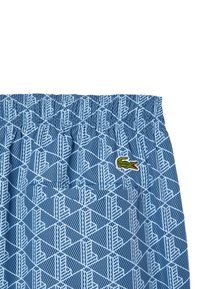 Bañador azul con estampado, con una cinturilla elástica, que presenta un diseño geométrico en blanco y un pequeño logotipo bordado de cocodrilo.