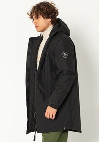 Zwarte hoodie-jack met een ritssluiting aan de voorkant, zijzakken en een logopatch op de mouw; heeft een gladde structuur en een middellange pasvorm.