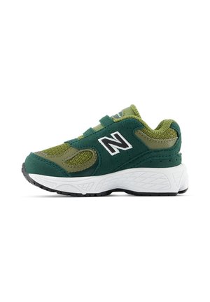 Baskets New Balance vertes et olive avec semelle blanche, dessus en mesh et en daim, et deux bandes Velcro, montrées de côté sur fond blanc.
