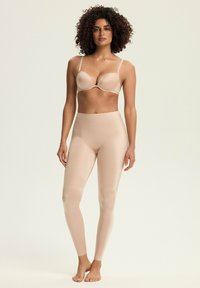 Beżowy zestaw stanika i legginsów, wykonany z gładkiego, elastycznego materiału o smukłym designie. Stanik ma regulowane ramiączka i formowane miseczki.