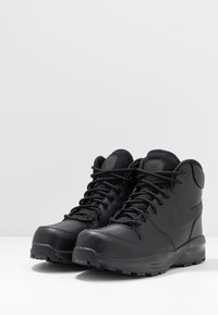 Black mid-top hiking boots made of synthetic material. Features sturdy laces, textured panels, and a rugged outsole for traction.