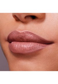 Couleur de lèvre nude sur des lèvres pulpeuses, avec une finition brillante, une texture lisse, une subtile teinte rose et une forme bien définie.