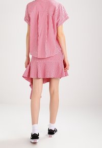 Robe à carreaux vichy rouge et blanc avec manches courtes, ourlet asymétrique et bas à volants, associée à des baskets noires et des chaussettes blanches.