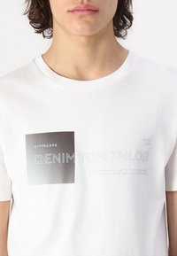 Valkoinen puuvillapaita, jossa mustat ja siniset graafiset printit, mukaan lukien "CITYSCAPE" ja "DENIM TOM TAILOR", pyöreä kaula-aukko.
