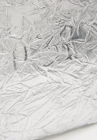 Skrynkligt silverfärgat metalltyg med en texturerad yta och oregelbundna mönster, som visar unika ljusreflektioner.