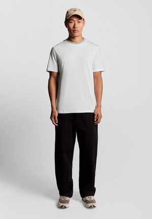 Vit kortärmad t-shirt, svarta löst sittande byxor, beige keps med logotyp och beige sneakers med grå detaljer. Enkel, avslappnad outfit.