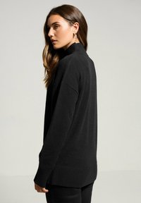 Schwarzer Pullover mit hohem Kragen, lockerer Passform, geripptem Saum und langen Ärmeln, gefertigt aus einem weichen, strukturierten Material.