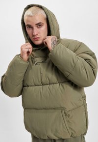 Olivgrüne, gepolsterte Jacke mit Kapuze, mit einer Vordertasche und dem Markenzeichen auf der Brust. Weicher, gestepter Stoff.
