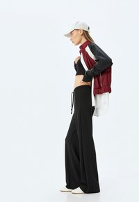 Sportig outfit med en vinröd och svart färgblockerad jacka, svarta vida byxor och en vit keps, med en croppad svart topp under.