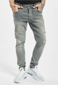 Harmaat revityt farkut, jotka on valmistettu denimmistä, sisältävät slim fit -mallin, viisi taskua ja näkyvää kulutusta; yhdistettynä valkoisiin lenkkareihin.