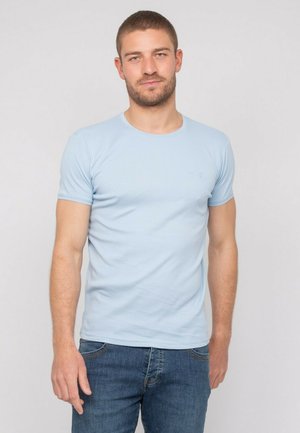 T-shirt en coton bleu clair avec un col rond, des manches courtes et un logo discret sur la poitrine. Coupe ajustée, texture lisse.