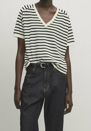 Striped v-neck t-shirt in cream and black, made of soft fabric, paired with dark denim jeans featuring a high waist and belt.