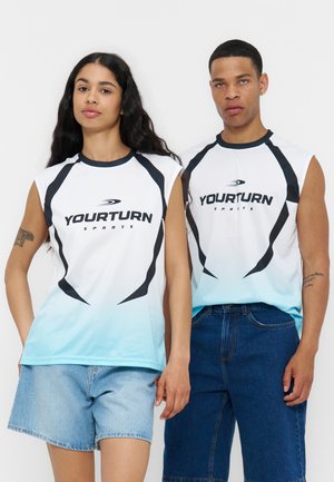 Dvaja modeli v bielych a modrých tielkach „Yourturn Sports“ bez rukávov, skombinovaných s džínsovými šortkami a džínsami, stoja na bielom pozadí.