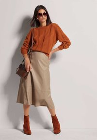 Roestkleurige gebreide trui, beige leren midi-jurk en roestkleurige enkellaarsjes. Een bruine crossbody tas en oversized zonnebril maken de look compleet.