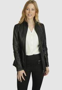 Black leather jacket with a stand-up collar and fitted sleeves, worn over a white button-up blouse and high-waisted black pants.