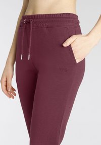 Kastanienbraune Baumwoll-Jogginghosen mit elastischem Bund, Kordelzug und Seitentaschen; mit gesticktem "H.I.S"-Logo auf dem Oberschenkel.