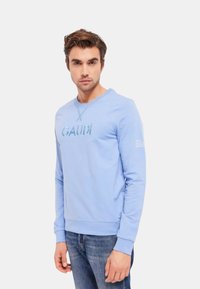 Felpa di cotone azzurro chiaro con collo a giro, maniche lunghe e logo stampato "GAUDI" sul petto. Presenta polsini e orlo a coste.