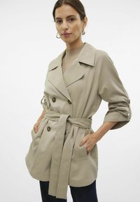 Chaqueta beige de doble botonadura con cinturón, grandes solapas, mangas con puños y dos bolsillos frontales. Tejido suave con un diseño estructurado.