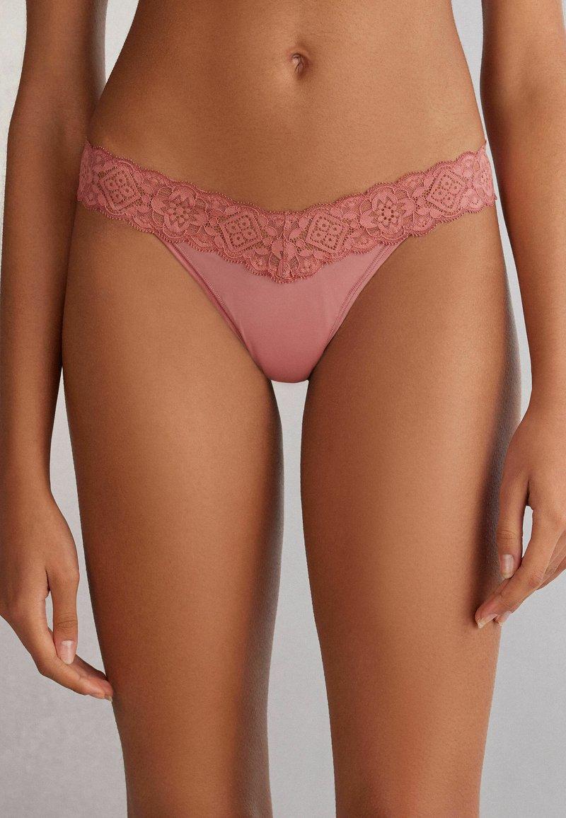 Rosa farbener String-Tanga mit einem floralen Spitzenbund, der über feine Muster verfügt, aus weichem Stoff und mit minimalistischem Design.
