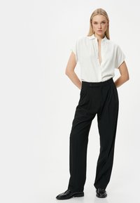 Camisa blanca de manga corta tipo botón combinada con pantalones ajustados negros de tiro alto, con cierre frontal de botones y tejido liso.
