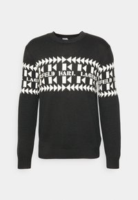 Czarny dziergany sweter z białym geometrycznym wzorem i napisem „KARL LAGERFELD” na wysokości klatki piersiowej. Posiada okrągły dekolt i ściągacze na rękawach.