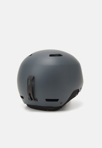 Casco grigio opaco con fori di ventilazione, cinturino regolabile e clip posteriore per una vestibilità sicura. Forma arrotondata progettata per sicurezza e comfort.