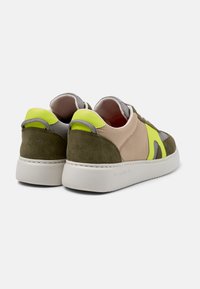 Sneakers featuring a mix of olive green suede, beige fabric, and bright yellow accents, white rubber soles, and looped heel details.