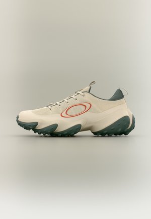 Scarpa da ginnastica sportiva beige chiaro con suola verde testurizzata, logo ovale arancione sul lato, tomaia in mesh e linguette di trazione su linguetta e tallone.