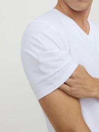 Fehér pamut V-nyakú póló, rövid ujjú, sima textúrával és testhezálló kialakítással. A váll és a kar területének közeli képe látható.