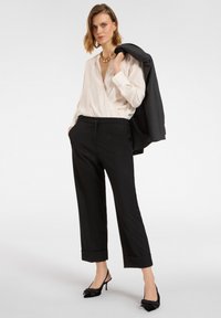 Czarne dopasowane spodnie z mankietami w zestawieniu z kremową jedwabną bluzką. Dodatki to złoty naszyjnik oraz czarne szpilki na odkrytej pięcie.