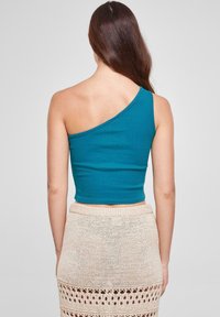 Teal ett-skulder crop topp i myk stoff, med en tettsittende design. Brukt med et beigemønstrete heklet skjørt.