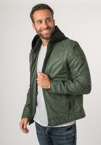 Giacca in pelle verde con fodera in felpa nera, chiusura con zip e tasche laterali. Texture liscia, vestibilità su misura e dettagli sottili sulle spalle.