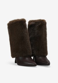 Botines de tacón con puntera afilada, que presentan una base de cuero marrón oscuro y una parte superior de piel de pelo marrón suave que se extiende hasta la pantorrilla.