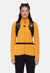 Helle orange Fleecejacke mit hohem Kragen und durchgehendem Reißverschluss, ausgestattet mit schwarzen Gurten, verstellbaren Beschlägen und reflektierenden Akzenten.
