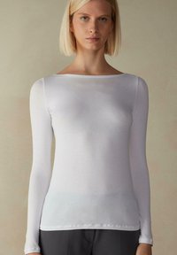 Hvid skjorte med lange ærmer lavet af et glat stof, der har en bred halsudskæring og en tætsiddende silhuet, med minimal syning i kanten.