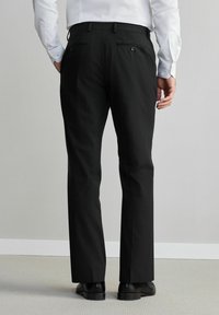 Pantalones negros de corte recto, con bolsillos traseros y una textura sutil, combinados con una camisa blanca y zapatos negros.