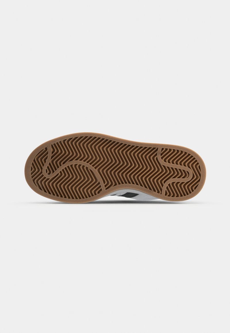 La suela del zapato presenta un diseño texturizado y estampado con un material de goma marrón, mostrando surcos en zigzag y una forma aerodinámica.