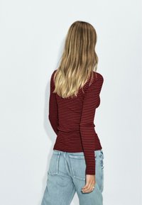 Red and navy striped long-sleeve shirt made of soft fabric, fitted design, paired with light blue high-waisted jeans.