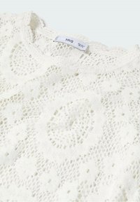 Biały sweter robiony na drutach z misternym wzorem koronkowym, dekoltem w łódkę i lekką teksturą. Logo marki widoczne w pobliżu kołnierza.