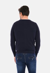Maglione girocollo blu navy con polsini e orlo a costine, realizzato in un tessuto a trama liscia. Design aderente mostrato dalla parte posteriore.