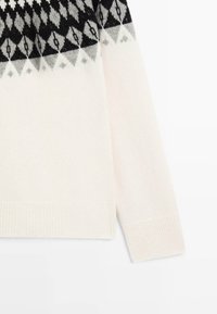 Gebreide trui in crème met een geometrisch zwart- en grijs patroon op het verspringende gedeelte, voorzien van geribbelde manchetten en zoom. Zachte textuur en ontspannen pasvorm.