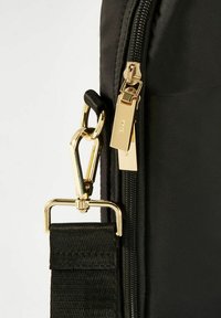 Czarna torba z złotym zamkiem błyskawicznym, wyposażona w złoty zamek do paska i teksturowany materiał. Podkreślona eleganckimi detalami hardware.