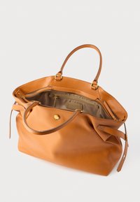 Ādas soma silti oranžā krāsā ar raupju tekstūru, divām rokturu siksnām un zelta krāsas pogas aizdari. Iekšpusē ir rāvējslēdzēja un ieliektās kabatas.