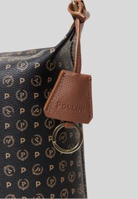 Borsa in pelle nera con texture, caratterizzata da un motivo con logo dorato e un'etichetta in pelle marrone con la scritta "POLLINI" in rilievo. Dettaglio in metallo dorato a forma circolare.