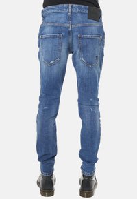 Jeans in denim blu skinny-fit con finitura scolorita, due tasche posteriori e una etichetta in vita nera. Il materiale sembra resistente con leggere scuciture.