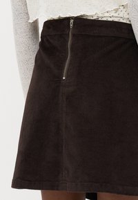 Jupe en velours côtelé marron avec une surface texturée, dotée d'une fermeture éclair sur le côté et d'une forme évasée, adaptée à un style décontracté.