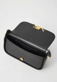 Black leather handbag with a gold hardware closure. Flat design, interior pocket, and adjustable strap. Smooth texture; minimalistic style.