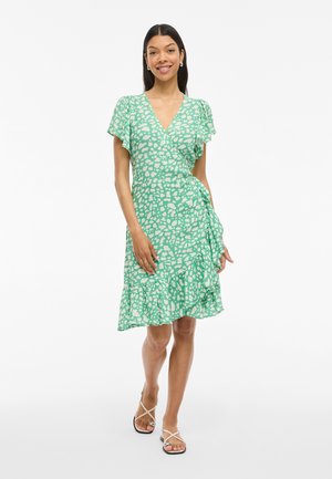 Robe portefeuille verte avec des motifs abstraits blancs, manches courtes à volants et ourlet en cascade. Fabriquée en tissu léger, longueur genoux.