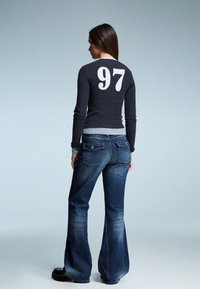 Sötétkék hosszú ujjú póló nagy fehér "97" felirattal a hátsó részen, párosítva bővülő kék farmerral és fekete platform cipőkkel.