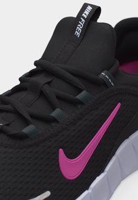 Chaussure de running Nike Free noire avec logo swoosh rose, lacets noirs et semelle blanche segmentée visible sur le côté droit.